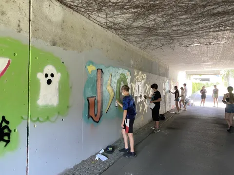 Jugendliche stehen an der Wand und sprayen farbige Graffitis. 